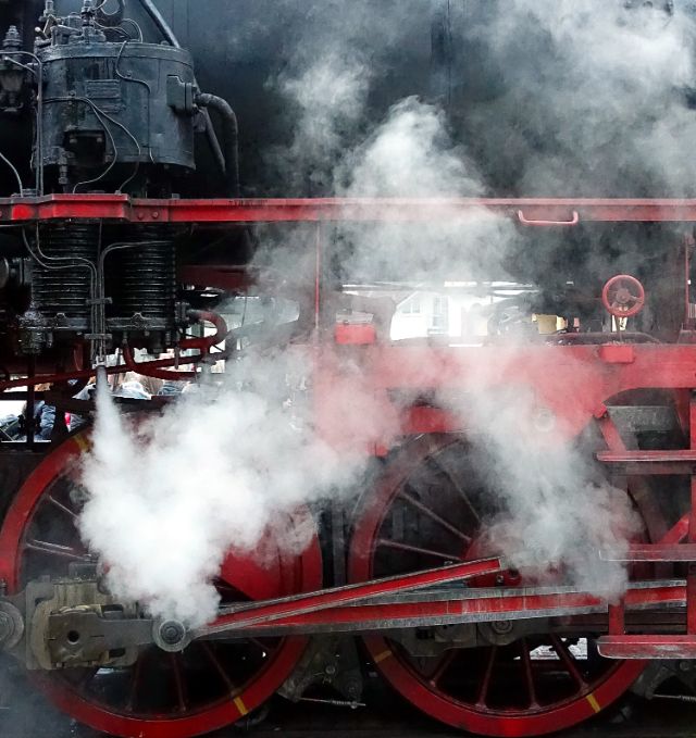 Eine rot-schwarze Dampflokomotive mit weissem Rauch