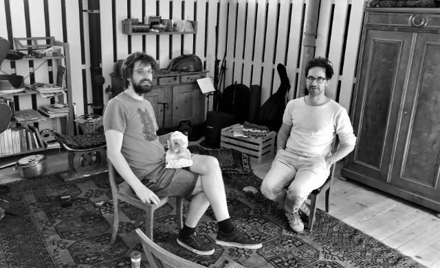 Robin Michel und Christian Moser sitzen gemütlich auf Stühlen vis a vis voneinander.