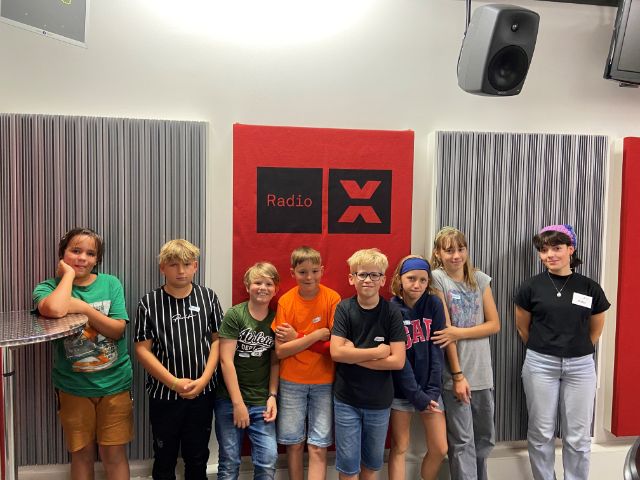 7 Kinder und eine Begleitperson stehen im Studio von Radio x für die Sendung vom Ferienpass.