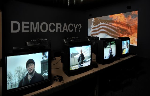 Different TVs in a dark gallery room with activists from around the world speaking.