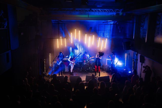 Eine Bühne in blau-goldenem Licht und spielenden Musiker:innen