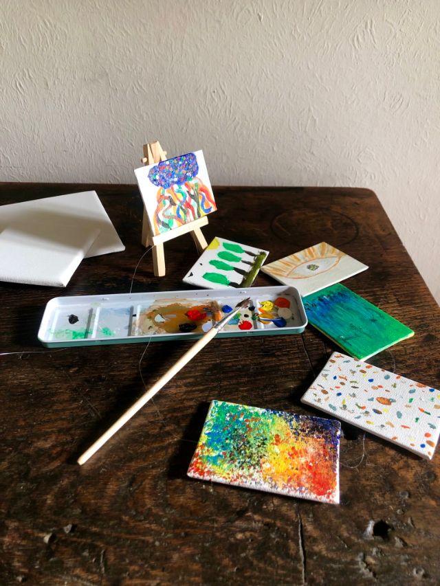 Bunte Kunstwerke auf Mini-Leinwänden, Malfarben und Pinsel auf einem Holztisch