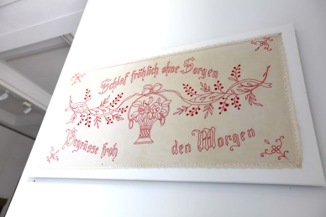 Ein Leinentuch mit einer Stickerei, ein Schriftzug mit "Schlaf fröhlich ohne Sorgen, begrüsse froh den Morgen"