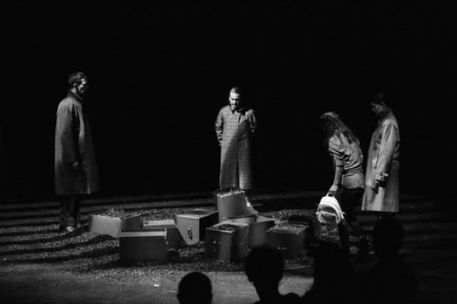 Theaterstück in schwarz/weiss, vier Figuren stehen auf der Bühne, ein paar Trümmer vor ihnen