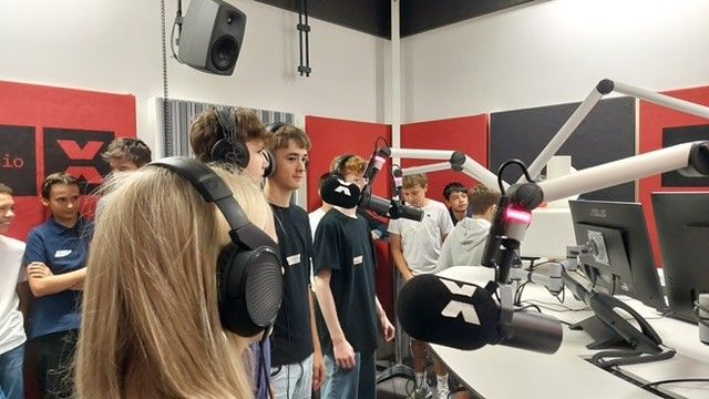 Jugendliche mit Kopfhörern stehen gespannt vor den Mikrophonen