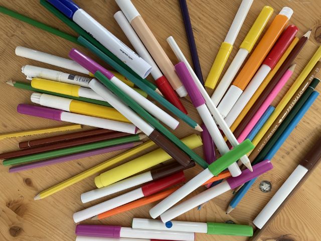 Farb- und Filzstifte unterschiedlicher Farben quer auf einem Holztisch verteilt