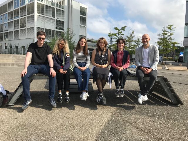 fünf Schüler:innen und ihre Lehrperson sitzen auf einer Bank in der Sonne