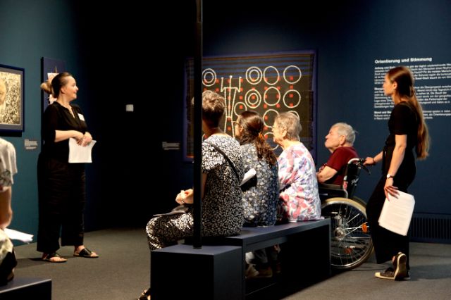 Zuhörende im Museum der Kulturen hören dem Ausstellungsguide zu