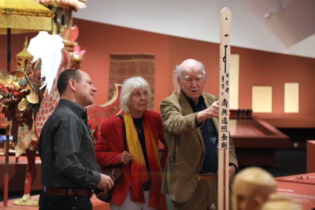 drei Menschen betrachten ein Exponat, ein mit japanischen Schriftzeichen beschriebenes Holz