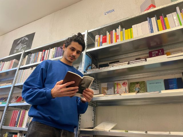 Ein junger Mensch schaut vor einem Lyrik-Regal in ein Buch