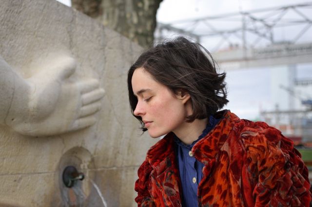 Eine Frau mit schulterlangen Haaren hat an einem Brunnen ihren Blick gesenkt