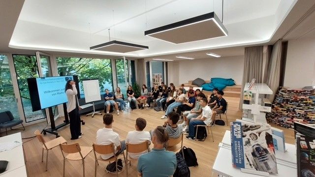 in der Schulbibliothek sitzen Schüler:innen vor einer Radiojournalistin, die einen Crashkurs erteilt