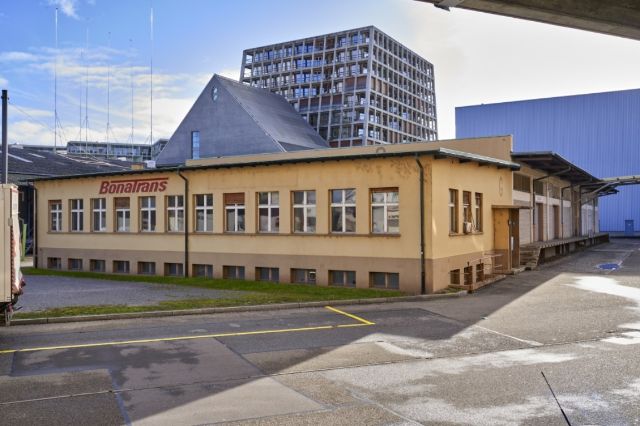 ein beiges Gebäude mit Bonatrans beschriftet, im Hintergrund ein Wohnblock und das Kunsthaus BL.