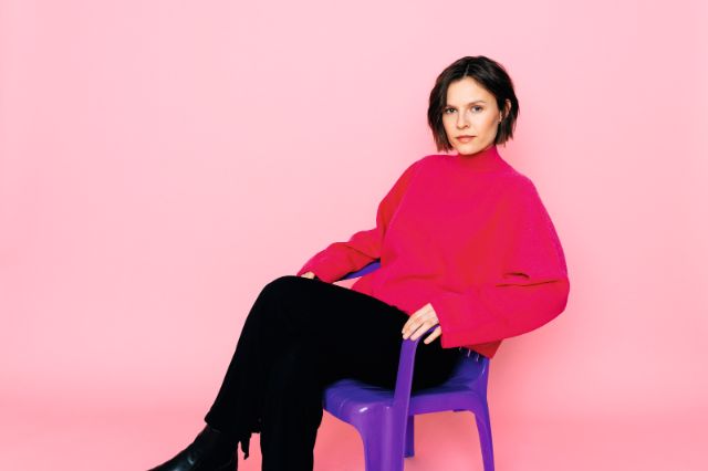 carla Kaspar sitzt auf einem violetten Stuhl und blickt in die Kamera
