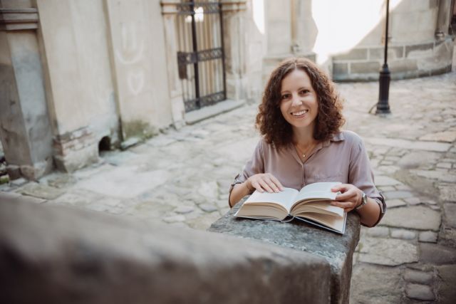 Eugenia Senik liest ein Buch in einem kleinen Gässchen mit Steinboden.