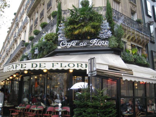 ein Strassenzug in Paris, im Vordergrund das Café de Flore mit weissen Storen und Café-Plätzen