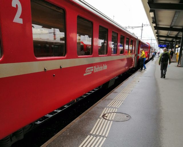 Ein roter Zug der Rhätischen Bahn steht im Bahnhof, Passagier:innen im Hintergrund