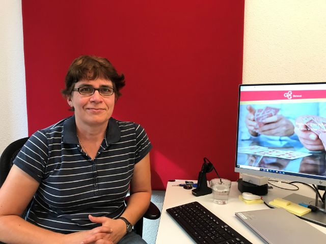 Eine Frau mit Brille sitzt an einem Bürotisch. Im Hintergrund ein Computer mit GGG Benevol