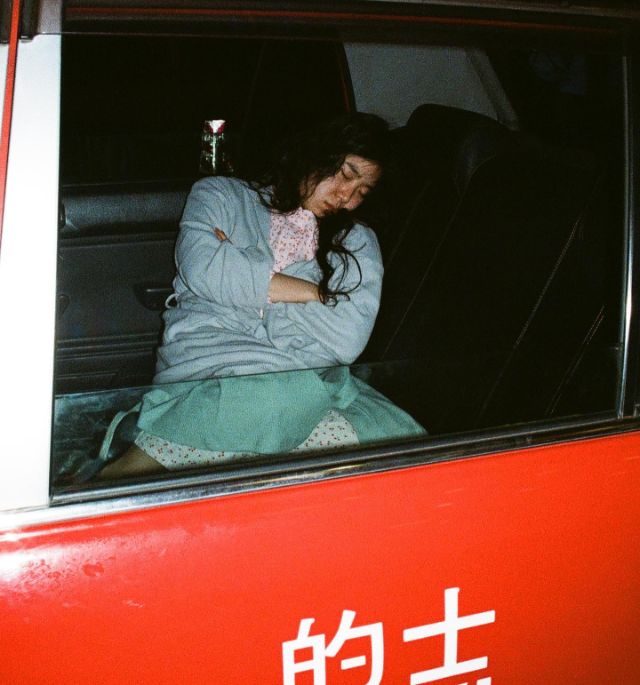 auf dem Hintersitz eines Autos liegt eine Person schlafend mit verschrànkten Armen