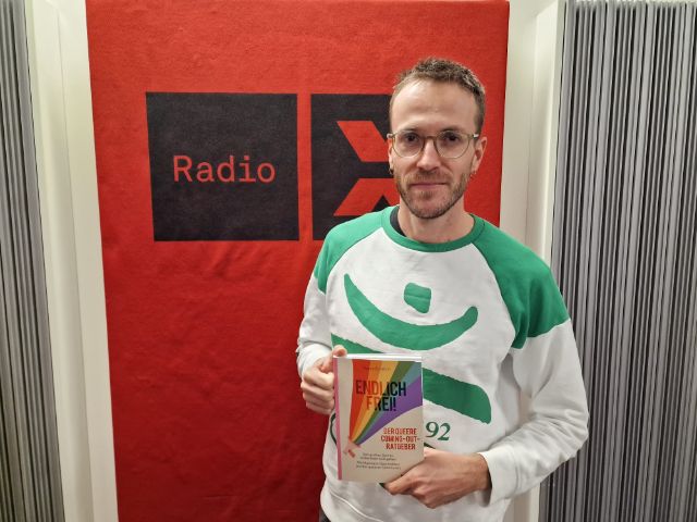 Marco Schättin hält sein Buch in der Hand und steht vor dem Radio X Logo im Radio X Studio.
