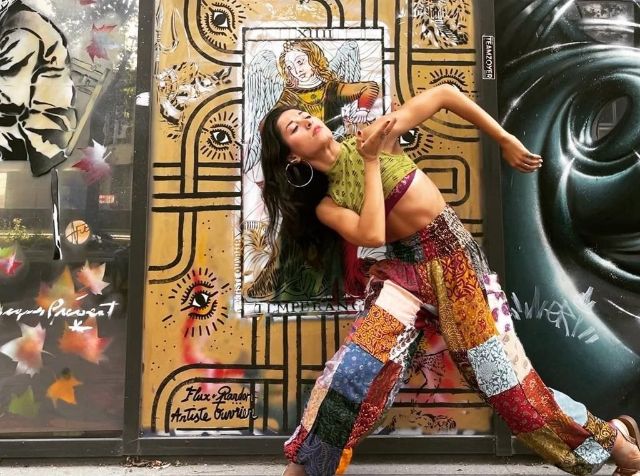 Eine Tänzerin mit farbigen Kleidern vor einer künstlerisch gestalteten Hausfassade