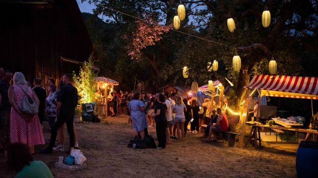 Menschen bei Abenddämmerung auf dem Festivalgelände mit Lampions und verschiedenen Ständen.