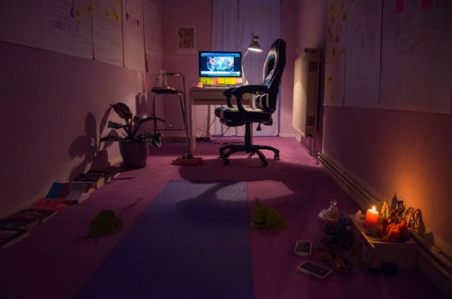 ein dunkel beleuchteter Raum zeigt einen Schreibtisch mit einem leeren Stuhl und einem leuchtenden Computerbildschirm.