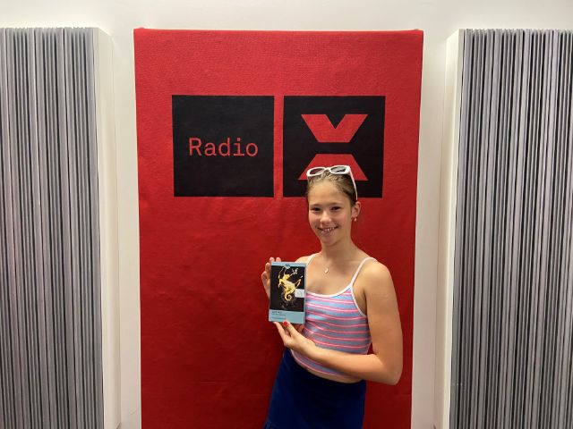 Sára Obmaščíková posiert mit dem Buch der 26 prämierten Texte vor dem Radio X Logo in unserem Studio.