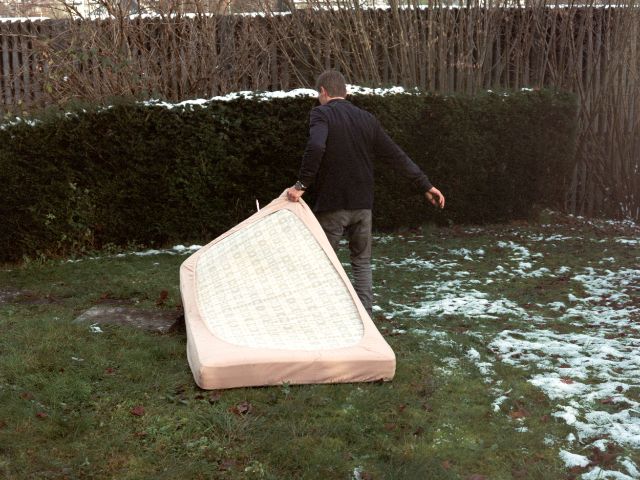 eine person zieht eine matratze hinter sich her auf einem leicht schneebedeckten rasen.
