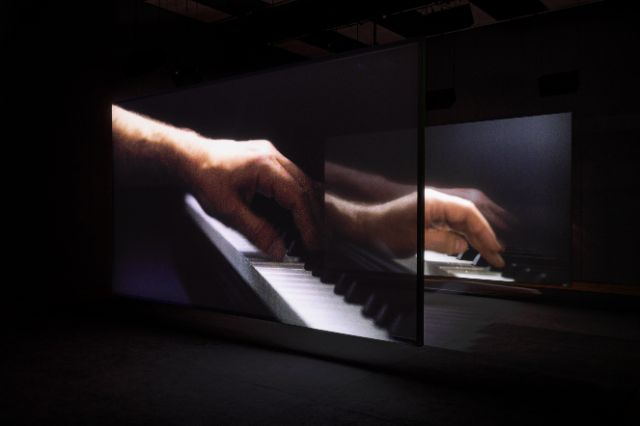 zwei projektionen zeigen zwei hände welche mit linker hand klavier spielen