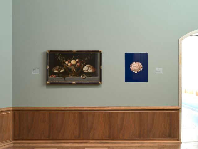 An der grünen Wand sind zwei Bilder zu sehen. Links ein klassisches Gemälde, rechts ein Bild von einem Laib Brot