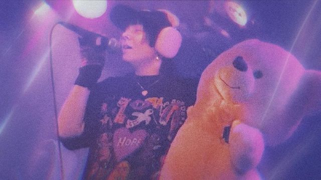 musiker*in mit mikrofon und kopfhörern in violettem licht mit einem teddybären