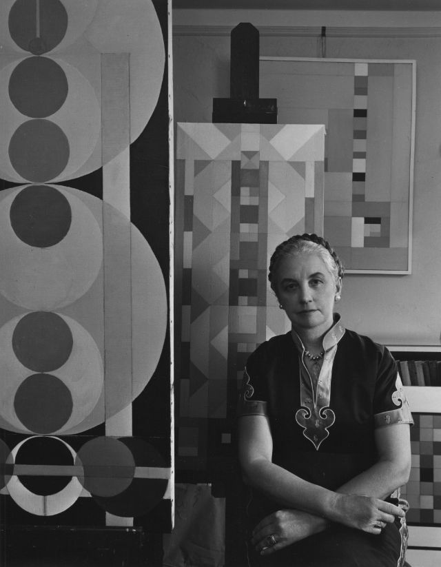 Portrait of American abstract painter Charmion von Wiegand (1896 - 1983) as she poses in her studio with several of her paintings, August 16, 1961  