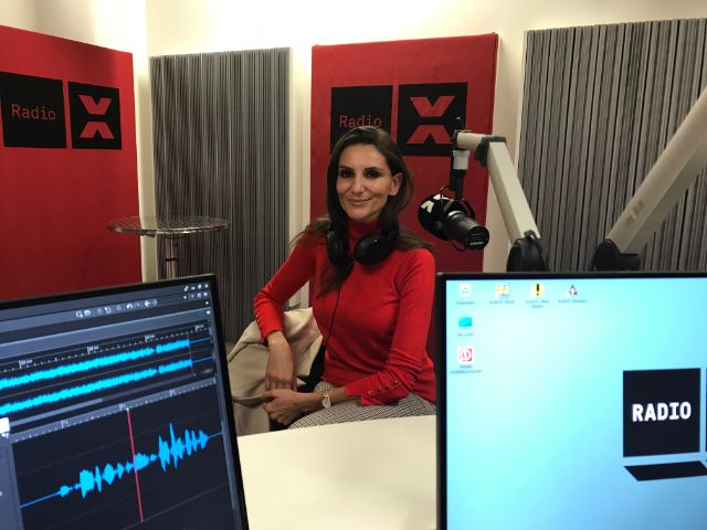 Eine lächelnde Frau in rotem Pullover sitzt im Studio von Radio X.