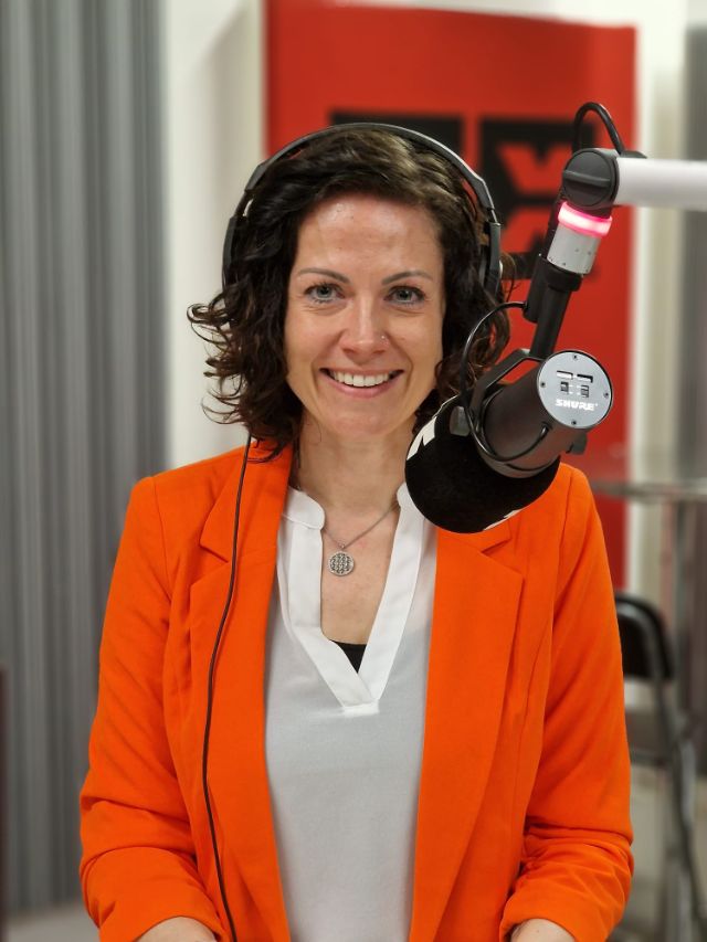 Tanja Mächler im Radio X Studio. Sie steht hinter dem Mikrofon und lächelt in die Kamera.