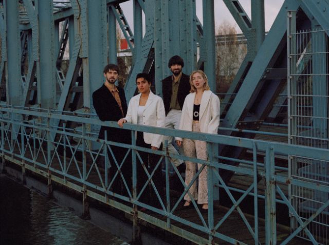 4 Menschen stehen auf einer rostblauen Brücke und schauen zur Kamera