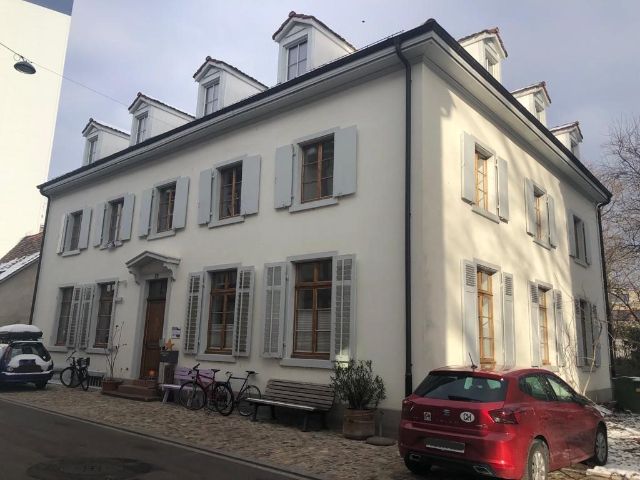 Ein altes zweistöckiges Haus mit weisser Fassade und grauen Fensterläden.