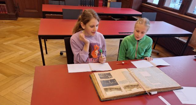 zwei Kinder diskutieren im Staatsarchiv über einem historischen Dokument 
