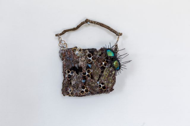 Eine Tasche aus Rindenstücken, Metallringen, einem Stock, einer Sonnenbrille und Nägeln.