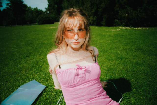 eine person mit sonnenbrille und kleid sitzt auf dem gras