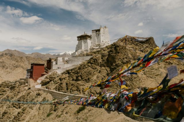 Berglandschaft in Tibet. Man sieht farbige Gebetsfahnen und einen Tempel im Hintergrund.