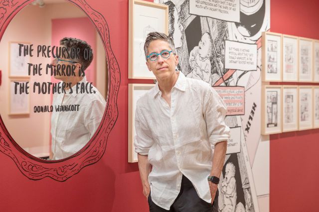 Alison Bechdel vor einem roten Hintergrund mit ihrer Kunst