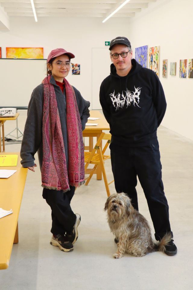 zwei menschen posieren mit hund vor kunst