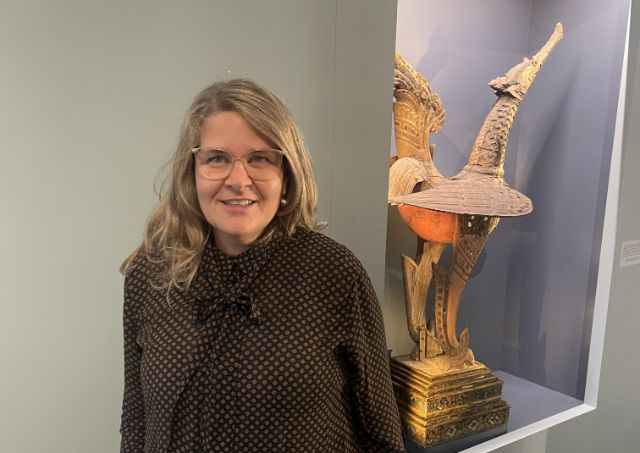 Eine Frau mit blonden langen Haaren und Brille vor einem Museumsexponat