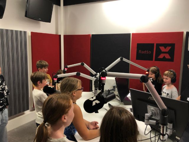 Eine Kindergruppe spricht begeistert im Radiostudio in die Mikrofone