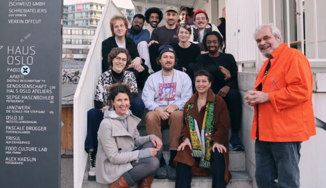 12 Personen sitzen und stehen auf der Treppe zum Studio