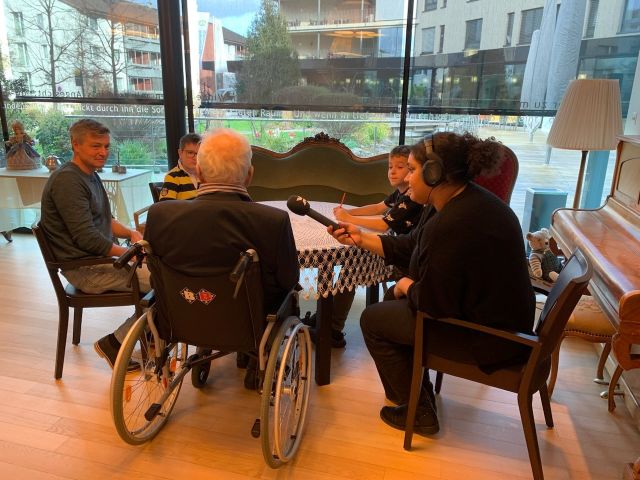 Eine Gruppe Menschen sitzt um einen Tisch herum, ein Senior in einem Rollstuhl