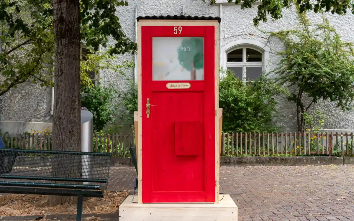 Installation aus Holz: Eine rote Tür mit Milchglasfenster. Wer sehen will, was sich dahinter verbirgt, muss die Tür öffnen.